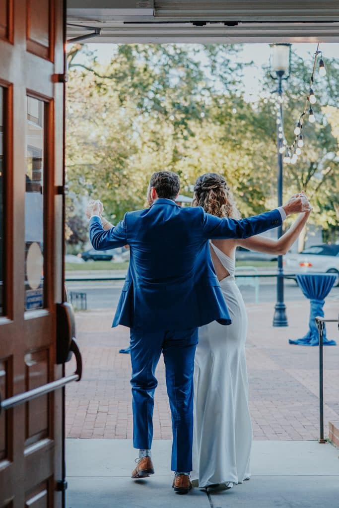 The backs of a Bride and Groom as they emerge from their wedding vow location at Eastern Market into the early evening on the patio.
